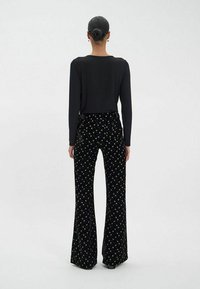 Haut à manches longues noir associé à un pantalon évasé noir avec un motif d'étoiles dorées, fabriqué en tissu doux et texturé.