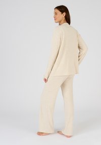 Set di loungewear beige a coste composto da una maglia a maniche lunghe e pantaloni a gamba larga, caratterizzato da una texture morbida e una vestibilità rilassata.