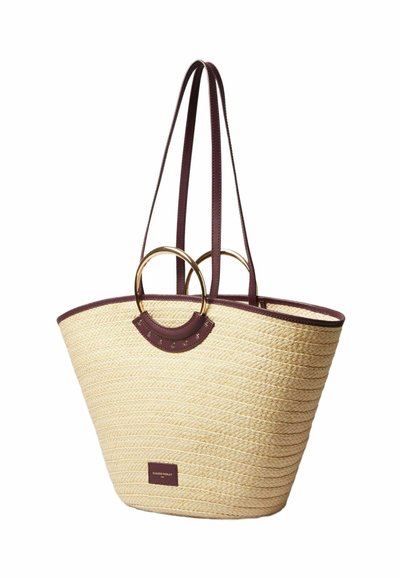 Sac en paille tissé avec des accents en cuir bordeaux, des anneaux en or circulaires et un design texturé ; dispose de deux longues sangles pour le porter.