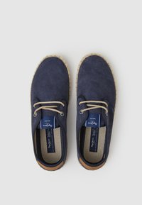 Chaussures en daim navy avec des lacets en corde beige, une semelle en espadrille texturée et une étiquette bleue à l'intérieur. Bout arrondi et design décontracté.