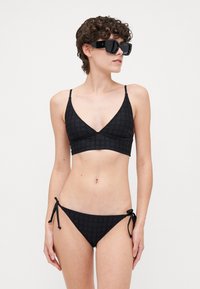 Ensemble de bikini noir à motifs, comprenant un bralette triangulaire avec de fines bretelles et un bas assorti avec des liens réglables sur les côtés.