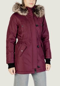 Giacca parka bordeaux con cappuccio in pelliccia sintetica, chiusura con zip e bottoni a pressione, vita elasticizzata e due tasche frontali con dettaglio a scatto.