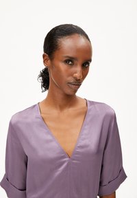 Lavender blouse with a V-neck and rolled sleeves. Smooth texture, minimalistic design, and no visible patterns or accents.