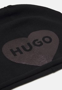 Berretto lavorato a maglia nero con un grande design a forma di cuore e la parola "HUGO" in grassetto nero. Tessuto morbido con una vestibilità aderente.