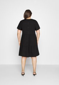 Schwarzes Baumwollkleid mit kurzen Ärmeln, gestuftem Rock und Knopfverschluss auf der Rückseite. Weiche Textur, knielanges Design.