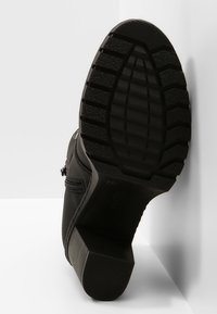 Bottine noire à talon épais avec un motif profond de semelle vu de dessous.