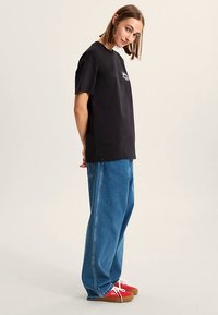 T-shirt noir en coton à manches courtes, logo à l'avant, associé à un jean denim bleu ample et des baskets rouges. Design minimaliste, coupe décontractée.