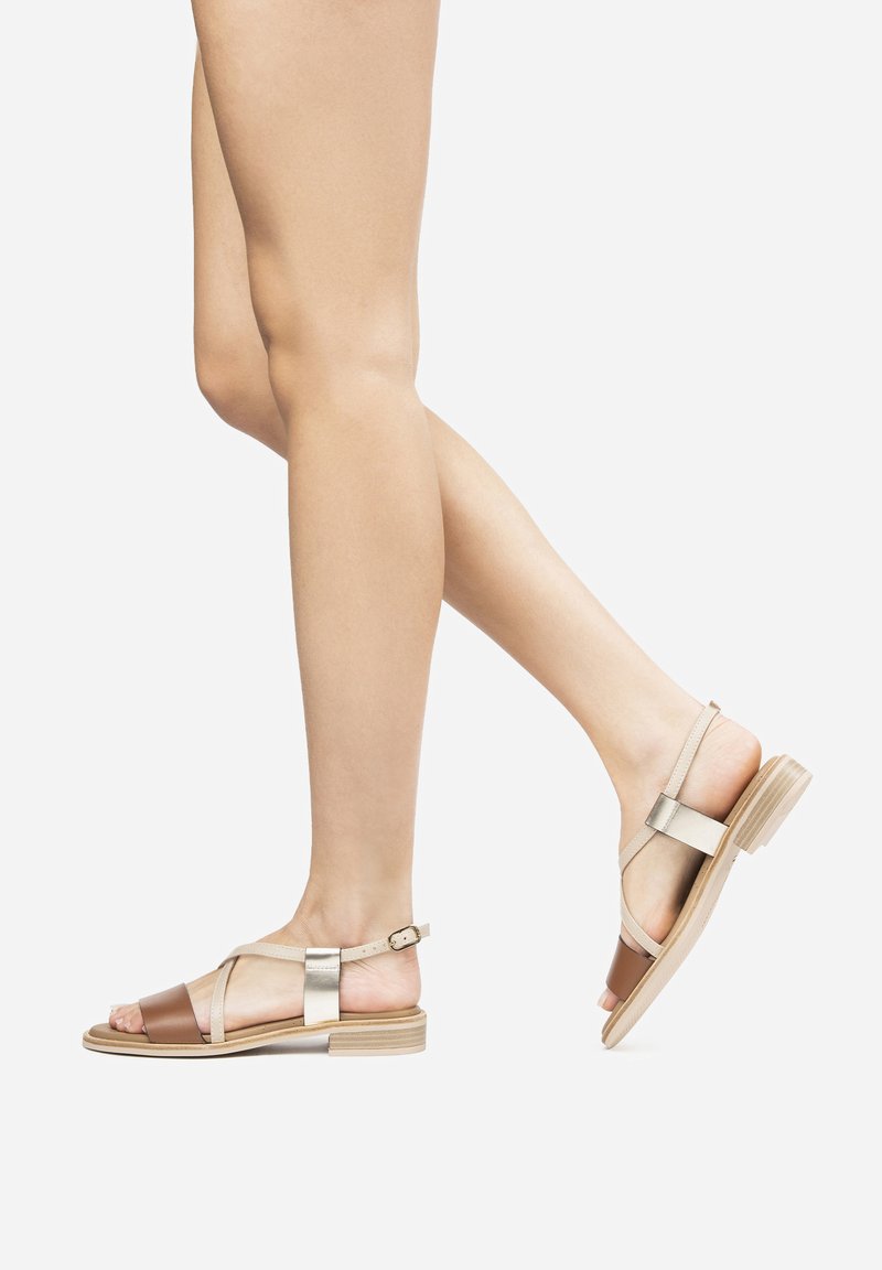 Sandali aperti con una combinazione di cinturini color cammello, nude e oro metallico. Suola piatta con un piccolo tacco e un chiusura a fibbia sulla caviglia.