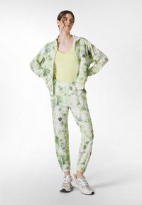 Lys grøn tie-dye træningsdragt med en lynlåslukket jakke, fitted bukser og en matchende gul top. Inkluder teksturerede sneakers med accenter.