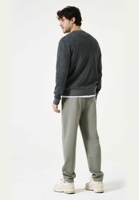 Grijze gebreide trui met een gemêleerd uiterlijk, gecombineerd met lichtgrijze losse broek. Schoenen zijn beige, met een chunky zoolontwerp.
