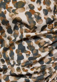 Textil mit einer strukturierten Oberfläche und beigem Hintergrund, das ein verstreutes Muster aus braunen, grünen und blauen kreisförmigen Formen zeigt und einen dynamischen visuellen Effekt erzeugt.