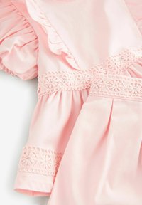 Robe rose avec des manches volantes, bordure en dentelle avec des motifs floraux, et une texture de tissu douce. La conception inclut des plis à la taille.