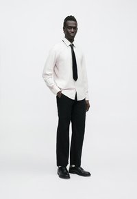 Bela in sivo črtasta srajca z gumbi, črna kravata, črne hlače in črni čevlji; vitka krojitev, gladka tkanina in krojena zasnova.