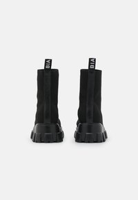 Bottes noires à cheville avec une tige en tricot texturé et une semelle en caoutchouc épaisse. Elles possèdent un tirette à l'arrière et une marque sur le talon.