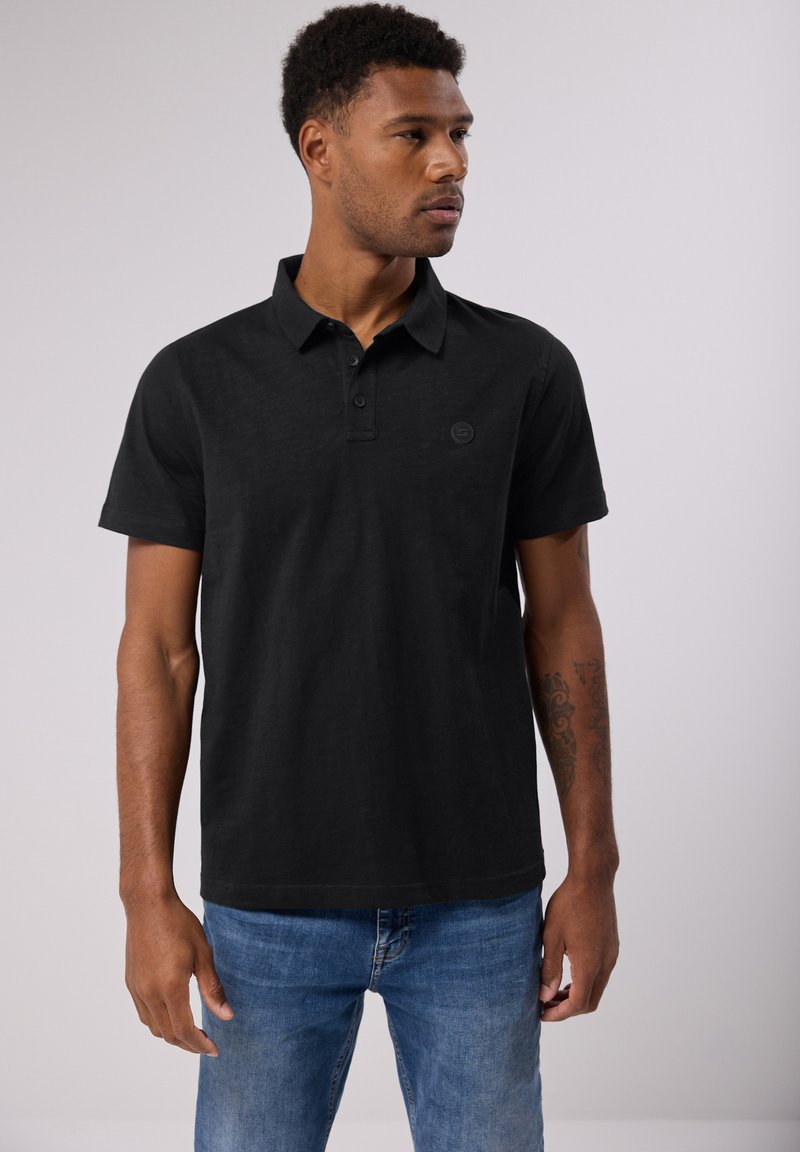 Paita polo musta, valmistettu teksturoidusta kankaasta, jossa on kaulus, kolme nappia ja pyöreä logo vasemmassa rinnassa.
