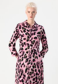 Šaty na knoflíky s růžovou tkaninou a vzorem černých a hnědých leopardích skvrn. Dlouhé rukávy a klasický límeček.