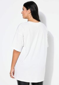 Witte oversized t-shirt met korte mouwen, met een ronde halslijn en een soepele textuur, gedragen met zwarte leggings, gezien vanuit de achterkant.