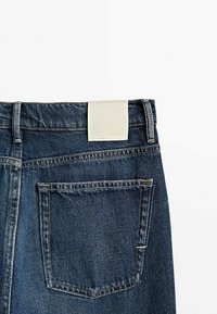 Mörkblå denimjeans med en vit läderetikett vid midjan och en enkel bakficka. Har synlig sömnad och en klassisk design.