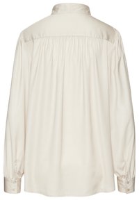 Blusa lunga beige chiaro con maniche lunghe, colletto, dettagli con pieghe sul retro e polsini con bottoni; tessuto liscio con una consistenza morbida.