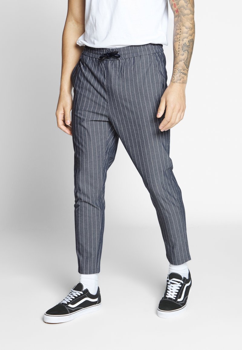 Grijze pantalon met streepjes, voorzien van een elastische tailleband en een trekkoord. Tapered fit met een zachte textuur. Gekocht met zwarte sneakers en witte sokken.