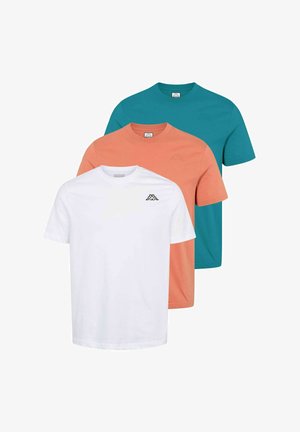 Fehér rövid ujjú pólót logóval viselő férfi, sötét cargo nadrág és fehér sportcipő, hátratett kézzel áll, és balra néz.