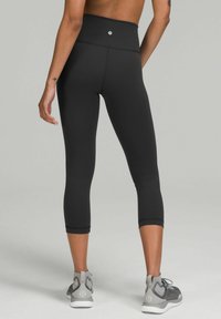 Zwarte high-waisted capri leggings gemaakt van rekbaar materiaal, met een naadloos ontwerp en een brede tailleband, gecombineerd met grijze sport schoenen.