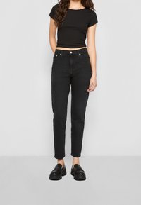 Jeans negros de cintura alta con corte ajustado, que cuentan con cinco bolsillos y detalles de costura sutiles, combinados con mocasines negros y un top negro corto.