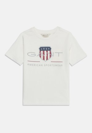Valge lühikeste varrukatega t-särk ümmarguse kaelusega, millel on punase, valge ja sinise kilbilogo, aastaarv "1949" ja tekst "GANT American Sportswear".