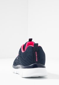Skechers treningssko med overdel i marineblå mesh, rosa interiør og hvit fleksibel såle. Har en drageløkke og logo på hælen.