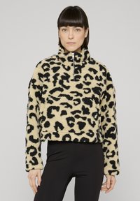 Gekürzter Fleecepullover in Beige mit schwarzem Leopardenmuster, hohem Kragen, Halbreißverschluss und langen Ärmeln. Strukturierte, weiche Materialqualität.