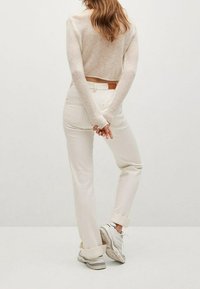 Jeans putih dengan potongan tinggi, rol di bagian bawah, dan saku belakang. Dipadukan dengan sweter panjang lengan yang ringan dan pas tubuh, serta sepatu sneaker.