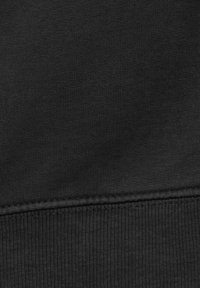 Gros plan sur un tissu noir montrant les coutures détaillées et la texture d'un ourlet côtelé sur un vêtement.