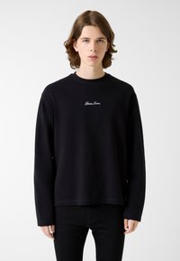 Czarna bluza z długim rękawem i okrągłym dekoltem, z bia�łym haftowanym logo "Gius Jeans" na piersi. Wykonana z fakturowanej tkaniny.