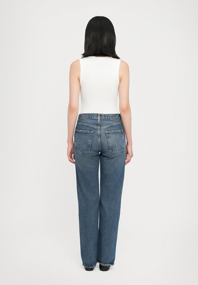 Haut léger blanc sans manches associé à un jean droit bleu taille haute avec poches arrière et une texture en denim classique.