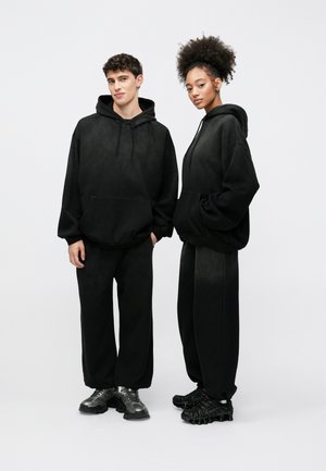 Black hooded sweatshirts with loose fit, paired with matching sweatpants. Models wear different black athletic shoes. Soft, plain texture.