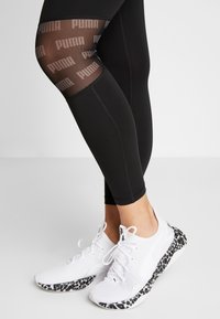 Leggings neri con dettaglio in rete del logo PUMA e cuciture a contrasto, abbinati a sneakers bianche con suola a stampa animale bianco e nero.