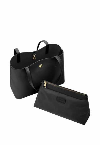 Črna usnjena torba tote z zlatim zaponkom in usklajeno črno torbico z zadrgo, postavljena spredaj na belem ozadju.