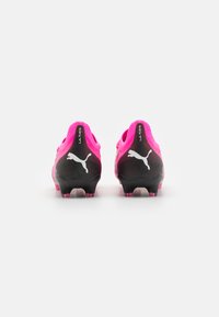 Puma nogometni kopački s ružičastim gornjim dijelom i crnim potplatom. Značajke uključuju teksturirani dizajn, oblikovane kopačke i bijele logotipne akcentacije.