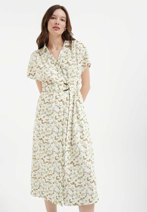 Leichtes, florales Wickelkleid mit kragenlosem Ausschnitt, kurzen Ärmeln, taillierter Passform und braunen sowie grünen Pflanzmustern auf einem cremefarbenen Hintergrund.