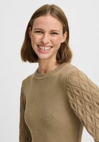Stickad tröja i ljusbrunt med ribbat kropp och texturerade ärmar i diamantmönster. Har en rund halsringning och en skräddarsydd passform.