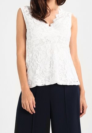 White lace sleeveless top featuring a scalloped neckline and floral pattern, worn over dark, wide-leg trousers. Smooth, textured fabric.