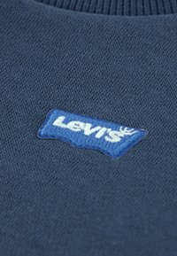 Tmavomodrý pletený sveter s textúrovanou nášivkou s logom Levi's v modrej farbe s bielym nápisom. Mäkká látka s rebrovaným výstrihom.