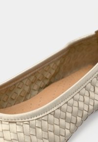 Μπαλαρίνα σε μεταλλικό μπεζ, με πλεγμένο δερμάτινο εξωτερικό, απαλό περίγραμμα και μαλακό καφέ εσωτερικό με οπές για διαπνοή.