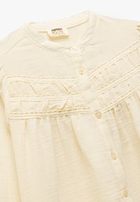 Lichtgele blouse met een knoopsluiting aan de voorkant, voorzien van een kantafwerking en geplooid ontwerp langs het lijfje. Zachte, lichte stof.