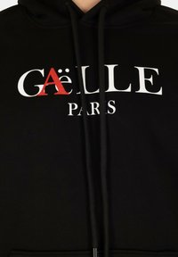 Felpa nera in cotone, con la scritta bianca "GAËLLE PARIS" e un accento rosso sulla lettera "A", dotata di cordini al collo. Design minimalista.