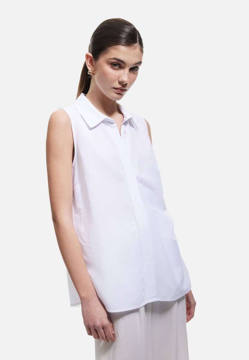 Weiße, ärmellose Bluse mit kragenförmigem Ausschnitt, vorderer Knopfverschluss und glatter Textur. Verfügt über eine lockere Passform und klare Linien.