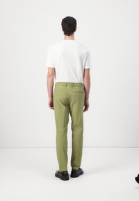 Pantalones de algodón verdes con un corte relajado, cintura elástica y un bolsillo trasero, combinados con una camiseta blanca lisa y zapatos negros.