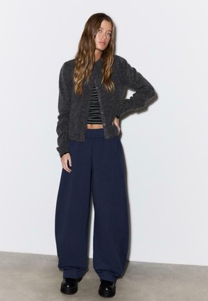 Cardigan in lana grigia sopra un top corto a righe bianche e nere, abbinato a pantaloni larghi color blu navy e scarpe con plateau nere.