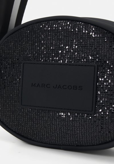 Zwarte tas bedekt met sequins, met een gladde zwartleren logo-patch waarop "MARC JACOBS" is gegraveerd, een afgeronde vorm en een gestructureerd oppervlak.