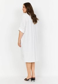Weißes, leichtes Hemdkleid, lockere Passform, dreiviertellange Ärmel mit aufgerollten Bündchen, seitliche Schlitze und ein gerader Saum. Einfaches, klares Design.